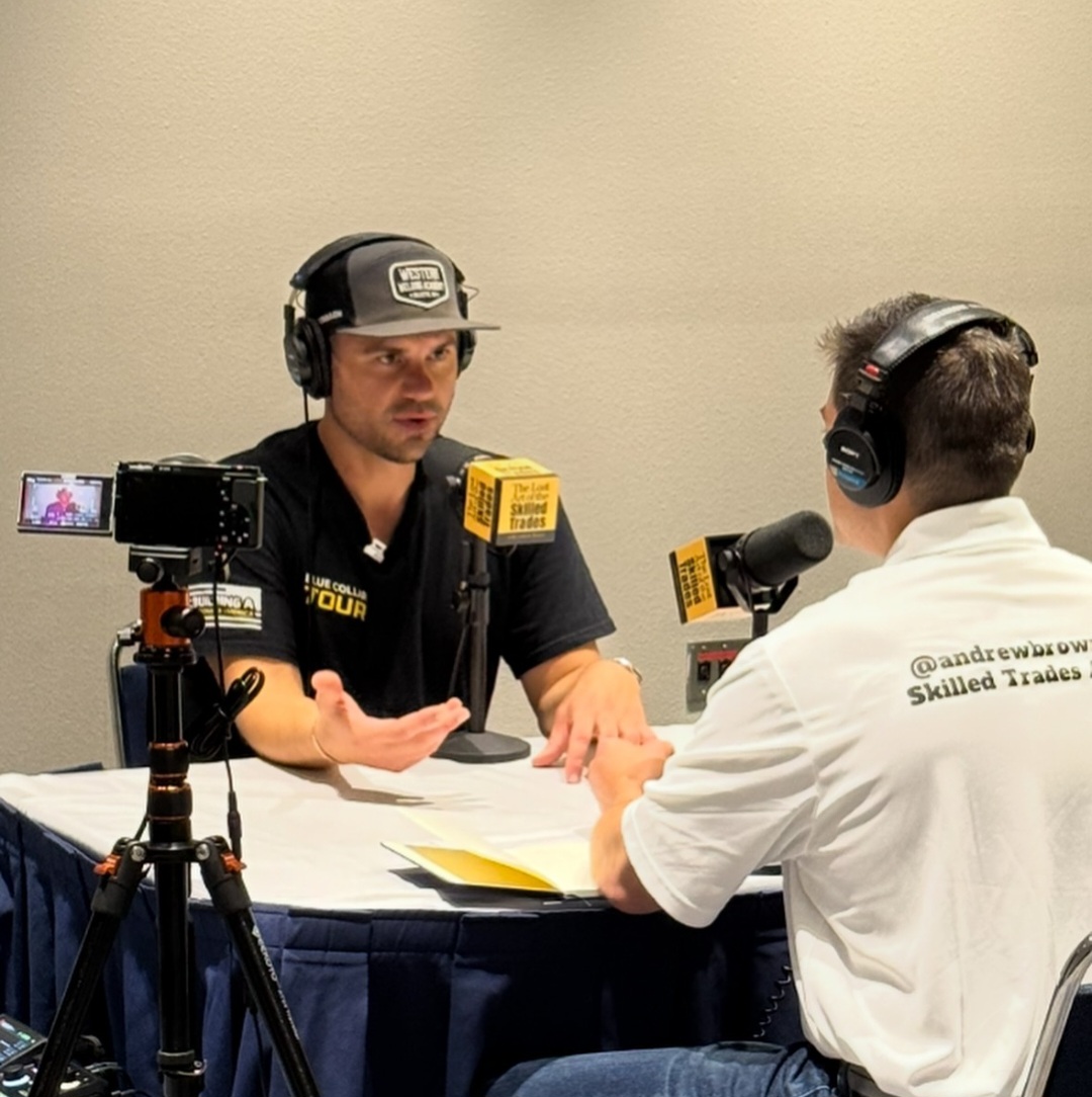 Andrew Brown interviewing a guest wearing headphones with branded microphones and a camera on a tripod